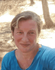 a woman wearing a blue shirt is smiling in front of trees