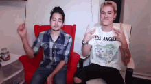 a man wearing a los angeles shirt is sitting next to another man in a red chair