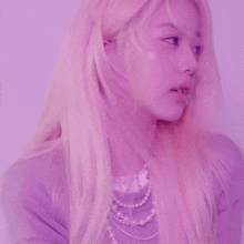 a woman with blonde hair and pearls is wearing a purple shirt and necklace .
