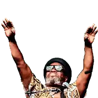 a man wearing sunglasses and a hat is singing into a microphone with his hands in the air