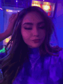 a woman in a purple shirt is standing in a dark room with purple lights behind her .