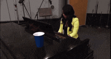 a woman is playing a piano with a blue cup on the keyboard