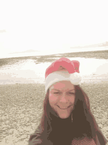 a woman wearing a santa hat is smiling on a beach