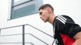 a man wearing a black and red adidas shirt is walking down a set of stairs