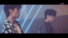 a man in a polka dot shirt stands next to another man in a dark room