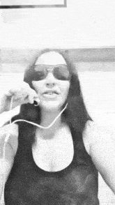 a woman wearing sunglasses and a black tank top is talking on a cell phone