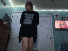 a girl wearing a black shirt that says this world stands in front of a television