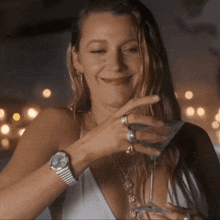 a woman wearing a watch is holding a martini glass and smiling