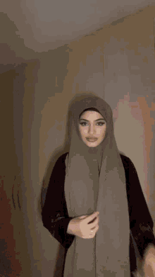 a woman in a hijab is standing in front of a wall .