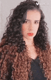 a woman with long curly hair and red lips is wearing a black dress and a fur vest .