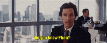 a man in a suit and tie is sitting at a table and says do you know plian
