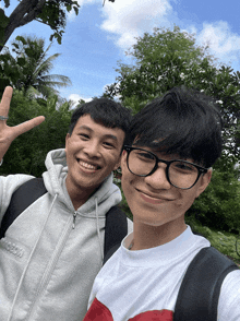two young men are posing for a picture with one wearing glasses and the other wearing a white shirt with a red heart on it