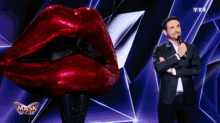 a man in a suit stands in front of a mask singer