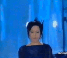 a woman in a black dress stands in front of a blue background that says rai