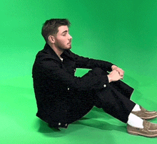 a man is sitting on the floor with his legs crossed in front of a green screen