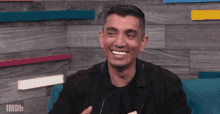 a man in a black jacket is smiling while sitting on a blue couch .