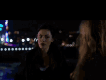 two women are looking at each other in a dark room with a blurred background