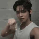 a young man in a white tank top is brushing his teeth with a soap bar .