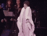 a woman is standing on a stage wearing a white fur coat .