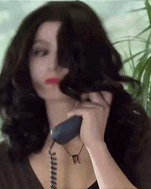 a woman is talking on a telephone with a necklace that has the letter r on it