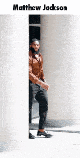 a man in a brown shirt and black pants is peeking out from behind a wall and the name matthew jackson is on the top