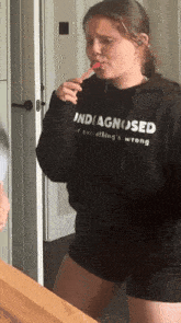 a girl is brushing her teeth and wearing a black hoodie that says ' undiagnosed ' on it