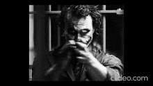 a black and white photo of the joker from the dark knight rises pointing his finger at the camera .