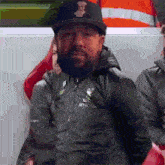 a man with a beard wearing a black hat and a jacket that says liverpool