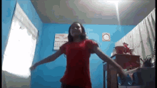 a girl in a red shirt is dancing in a room with a calendar on the wall behind her .