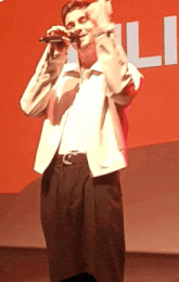 a man singing into a microphone in front of an orange background with the letter l