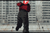 a man in a red jacket is running in front of a building with a play button on his back