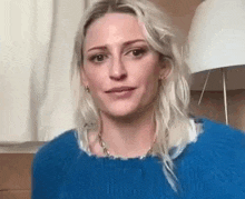 a woman wearing a blue sweater and a necklace is making a funny face .