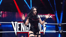 a woman stands in a wrestling ring with the word vengeance on the wall behind her