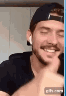 a man with a beard wearing a hat and ear buds is smiling and laughing .