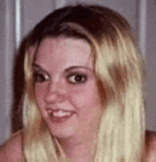 a close up of a woman 's face with long blonde hair and a smile .