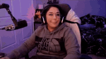 a woman is wearing headphones and a hoodie while sitting in a chair in front of a microphone .
