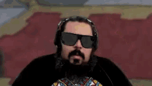 a man with a beard and sunglasses is wearing headphones and a black shirt .