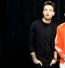 a man in a black shirt and a man in an orange jacket are standing next to each other .