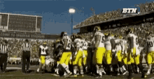 a group of football players huddle on a field with the btn logo in the background