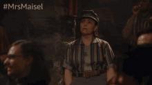 a woman in a striped shirt and hat stands in a crowd with the hashtag #mrsmaisel