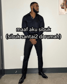 a man in a black suit is standing in front of a wall with a caption that says maaf aku sibuk