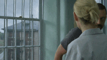 a man and a woman are standing in front of a window with bars on it