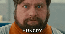 a man with a beard is looking at the camera with the words `` hungry '' written on his face .