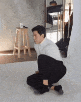 a man wearing a white turtleneck sits on the floor