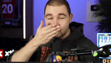 a man covering his mouth with his hand in front of a microphone with the number 20 on the wall behind him