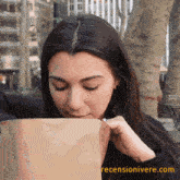 a woman smells something in a brown paper bag with the website recenzionivere.com in the bottom right corner