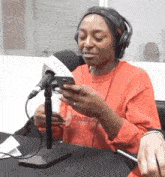 a woman wearing headphones and a red shirt is sitting in front of a microphone looking at her phone .