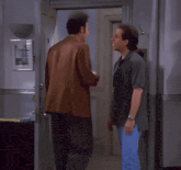 two men are standing next to each other in a hallway and shaking hands .