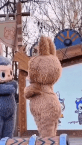two stuffed animals are standing next to each other in front of a sign .