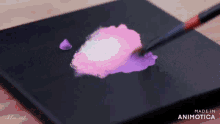 a brush is being used to apply pink and purple paint on a black surface